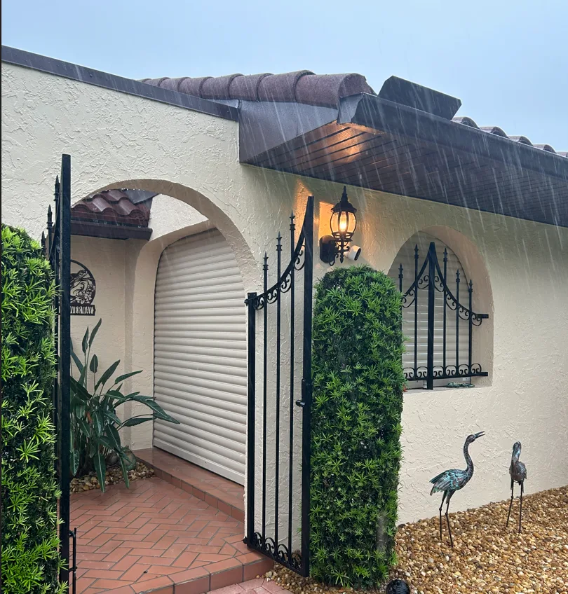 Beige roll-down hurricane shutter closed over an entry archway during heavy rain