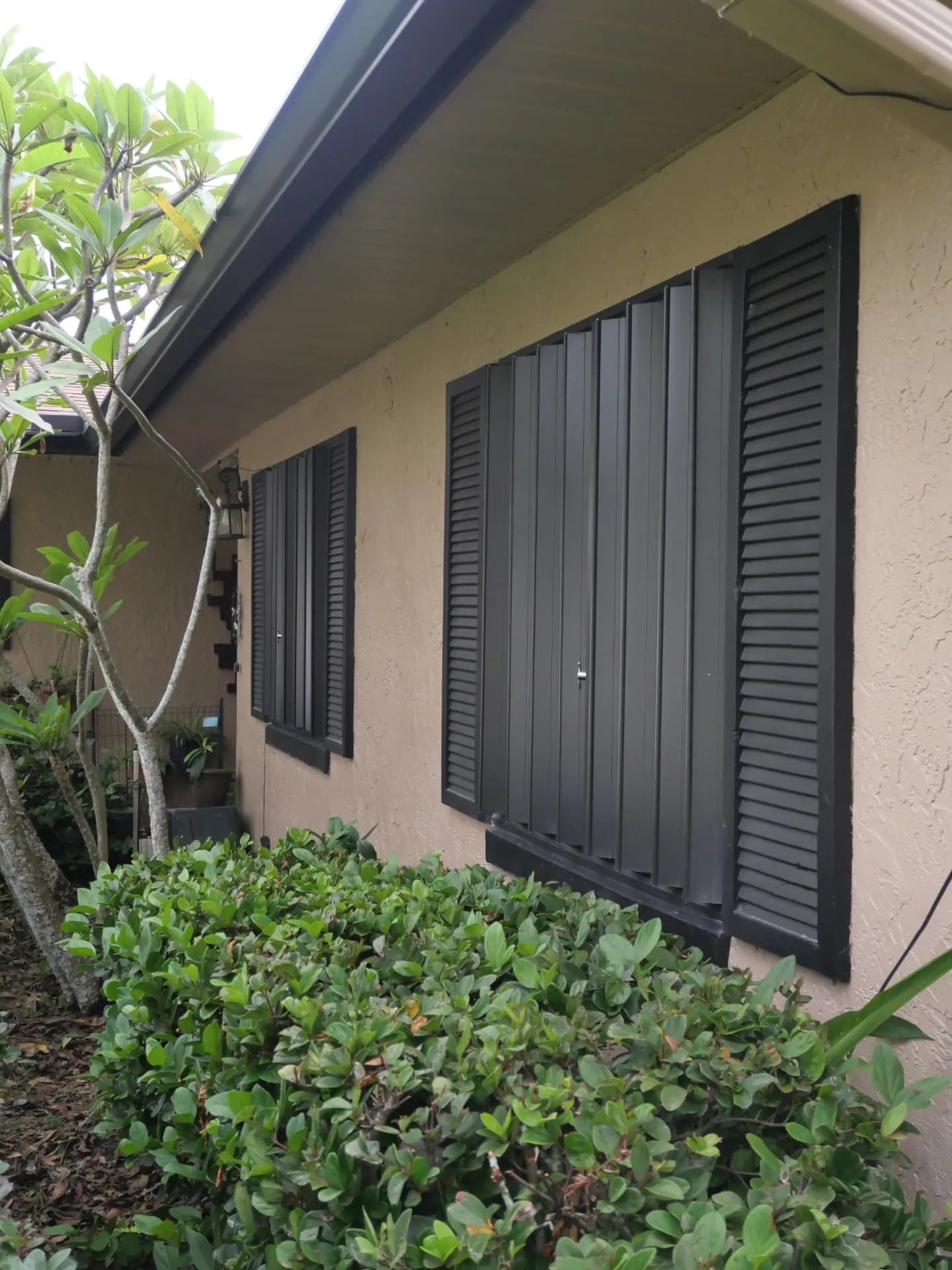 Bronze accordion hurricane shutters closed inside the window sills of a stucco home