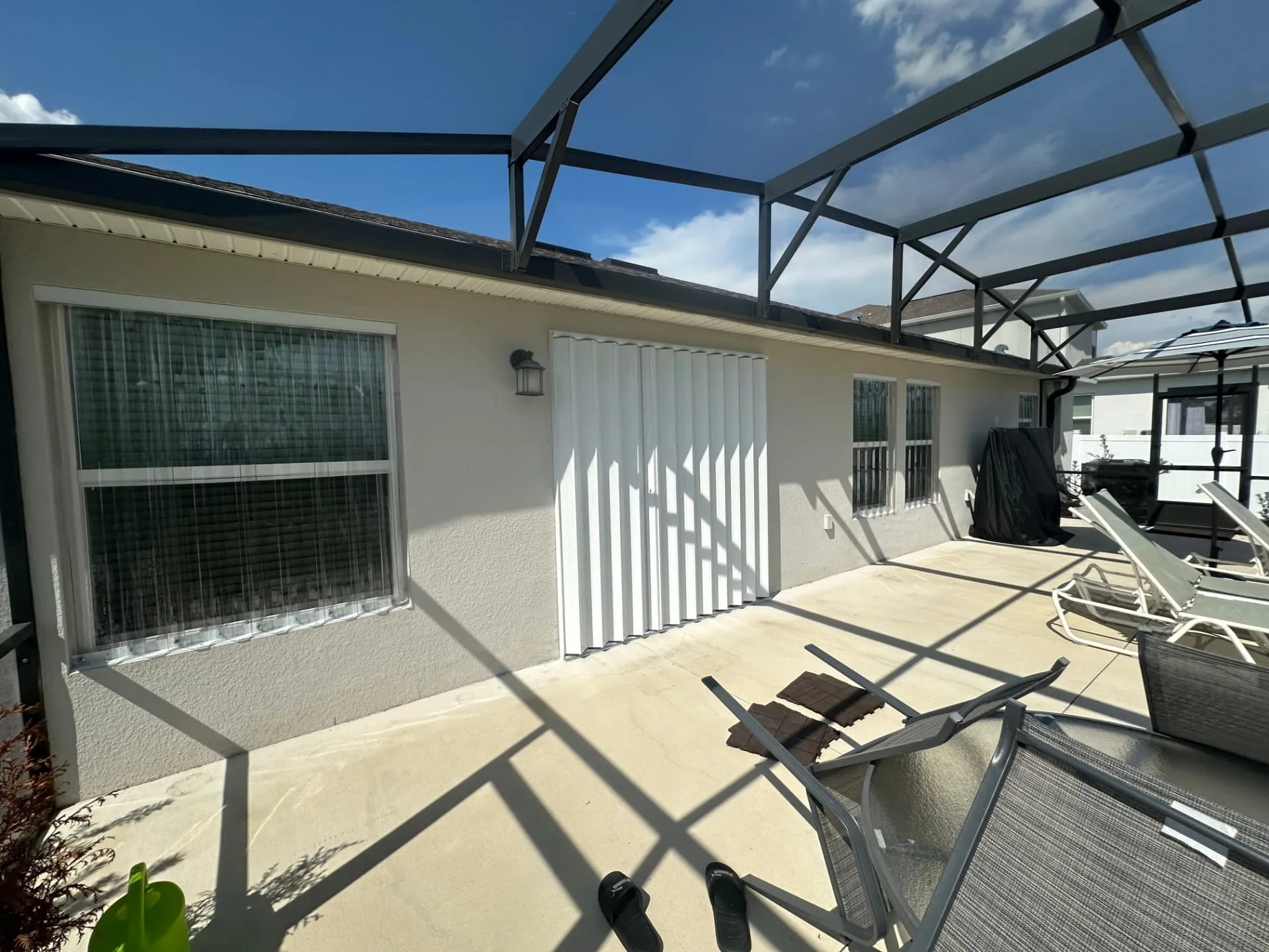 Clear polycarbonate storm panels on a lanai window beside a closed white accordion shutter