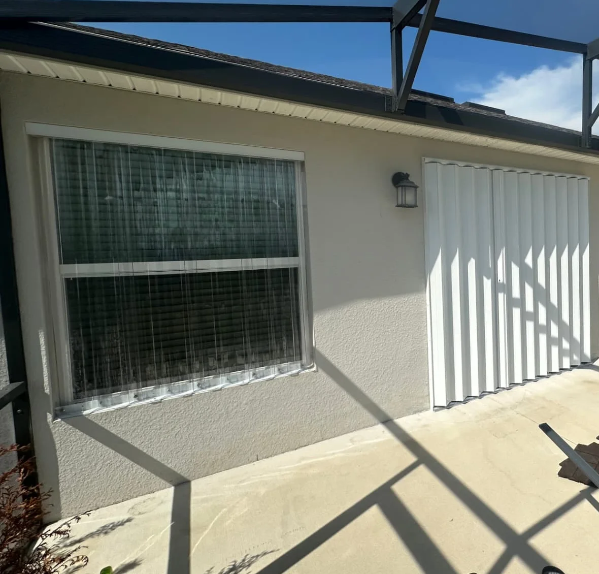 Clear polycarbonate storm panels fitted over a lanai window, with a closed white accordion shutter covering the door alongside it